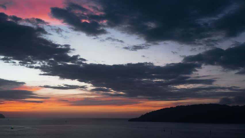 Aerial view of a dramatic colorful sunset sky with orange and pink clouds above the calm sea and silhouetted islands of the Kota Kinabalu waterfront