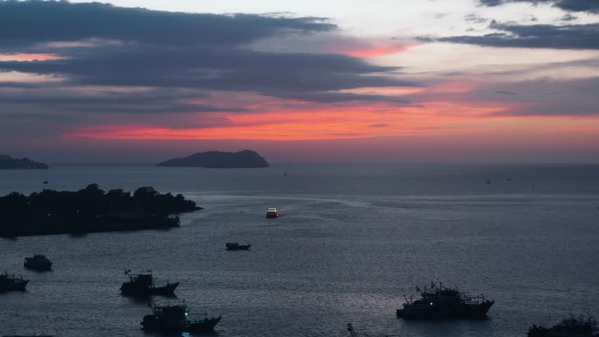 Fleet of silhouetted fishing boats on calm sea during a dramatic pink and orange sunset over Kota Kinabalu harbour with distant islands on the horizon