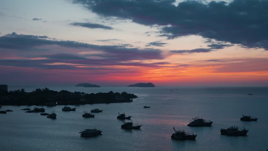 Scenic aerial panorama of Kota Kinabalu harbour at sunset shows a fleet of silhouetted fishing boats on calm sea with a dramatic orange sky and distant islands