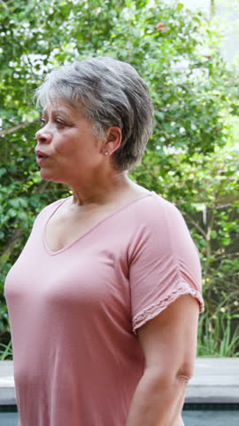 Vertical video: Mature female friends pausing on shoulder tap then laughing together in garden. Outdoors, companionship, natural, candid, joyful, relaxed, vertical video