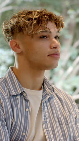 Vertical video: Male in early 20s at cafe seeing motion at window turning head smiling to greet pal. Contemplative, candid, natural, warm, relaxation, outdoor-inspired, vertical video