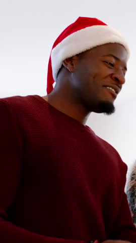 Vertical video: African American man wearing Santa hat leaning in offering after greeting in home. Festive, cheerful, candid, warm, joyful, celebration, vertical video