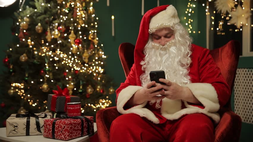 Santa using smartphone near Christmas tree sending holiday greetings.