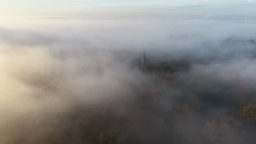 Church steeple rises through misty morning fog Epping Forest UK drone,aerial