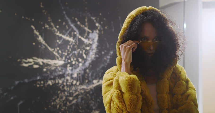 Woman in yellow fur coat posing confidently in stylish grunge studio. Fashion, style, clothing, confidence, urban, edgy