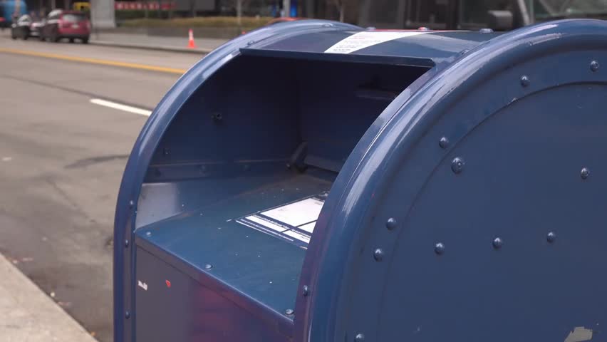 Tax documents being dropped into a public USPS mailbox, illustrating financial responsibility, mailing, and government services in 4K.