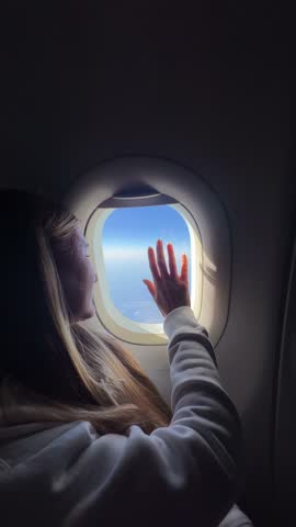Young woman dreaming while touching airplane window and gazing at bright sky during peaceful flight