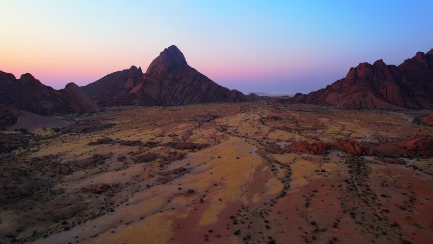 Granite peaks in warm sunset light with pink and blue sky over the Namib Desert, Namibia. Low aerial view