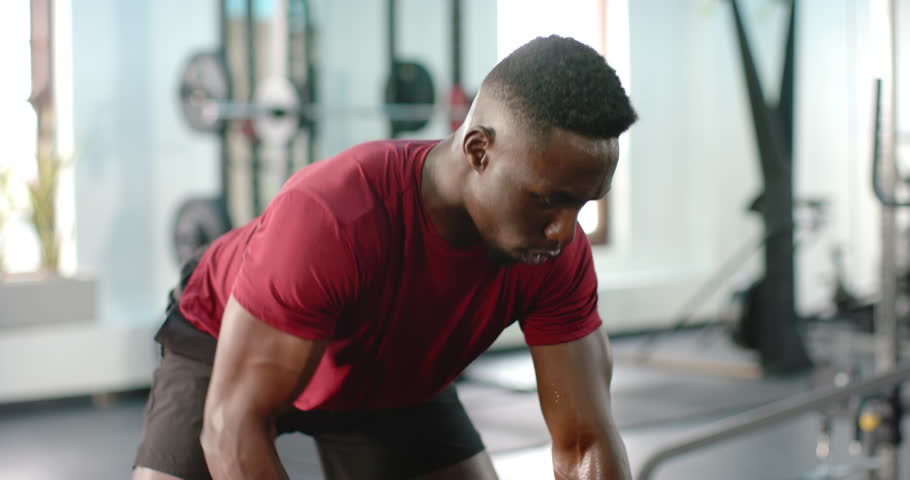 African American man leaning and gripping dumbbell on bench and rowing for strength in gym. Fitness, strength, workout, physique, training, exertion, athletic