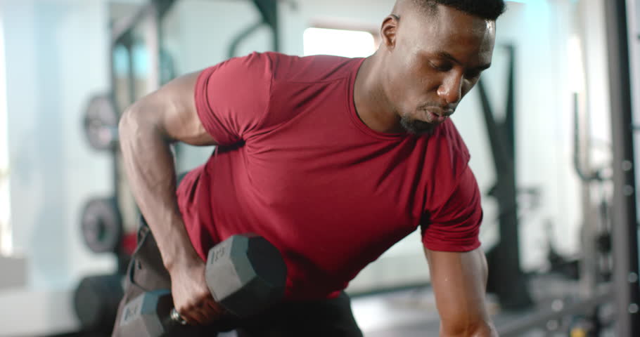 Spotting dumbbell, African American man rowing for strength in gym then checking smartwatch. Strength, fitness, training, athletic, determination, motivation, workout