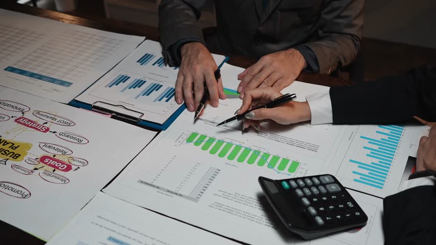 Professional analysts discussing and pointing at graphs and financial reports during a corporate meeting