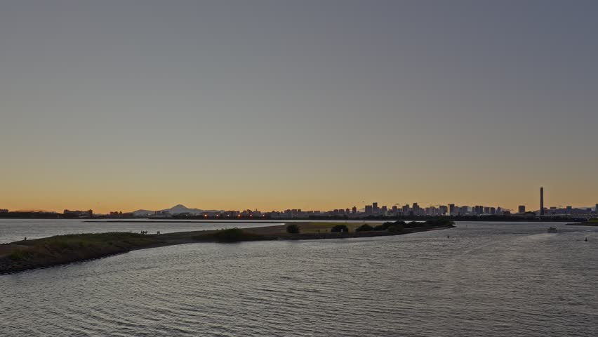 A wide view of Tokyo Bay, a breakwater, the distant city skyline, and the silhouette of Mount Fuji at civil twilight.