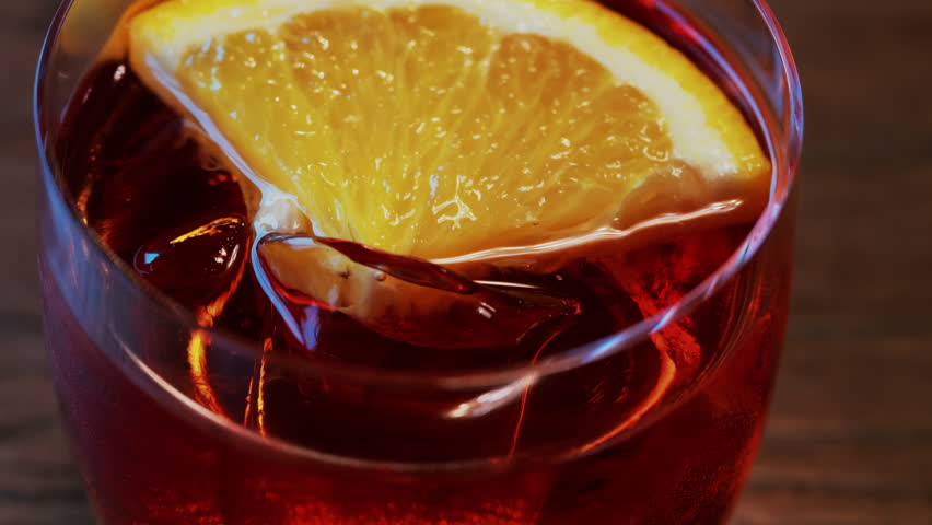 Close up of a Negroni cocktail with orange slice and ice cubes on a wooden table