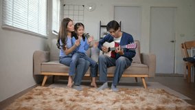 Joyful asian family spending quality time together, with the father playing guitar and the mother and daughter singing along on the sofa - Powered by Shutterstock - Get 15% off with code: PIKWIZARD15