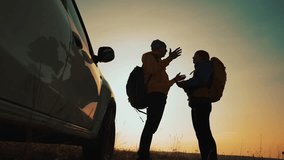 Discussing route two hikers stand beside car at sunset each hiker checks map and phone silhouette of couple with backpack near vehicle on grassy hill travel adventure planning under warm sky - Powered by Shutterstock - Get 15% off with code: PIKWIZARD15