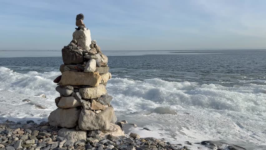 Video of Baikal Lake on sunny frosty December day. Stone pyramid of tourists on shore and white ice floes near blue water during freeze-up. Typical Baikal lakeside landscape. Winter travels concept