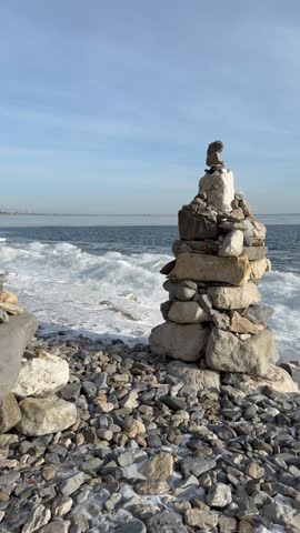Vertical panoramic video of Lake Baikal shoreline on a sunny, frosty December day. A stone pyramid built by tourists on coast and white ice floes at water edge during freeze-up. Winter travels concept