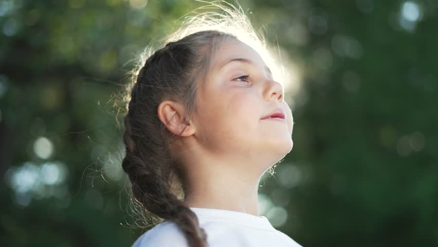 Girl breathes in warm sunlight as nature surrounds her in backlit portrait with braid in hair and serenity on face showing relaxation and child joy in outdoor soft sunbeam sunlit glow and breeze
