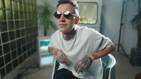 Trendy rap artist posing in studio, shooting music video, portrait indoors. Handsome young male person with tattoos, self-confidence and narcissism, contemporary art interior in studio, modern fashion - Powered by Shutterstock - Get 15% off with code: PIKWIZARD15