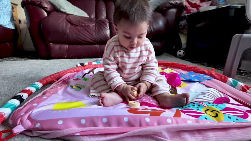 South Asian baby sitting on a colorful play mat and holding a wooden block