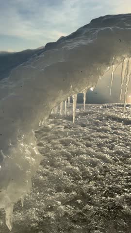 Vertical panoramic video of Baikal Lake during freeze-up on December sunny frost morning. Ice arch with icicles on icy beach on cold sunrise. Unusual winter landscape. Nature background. Winter travel