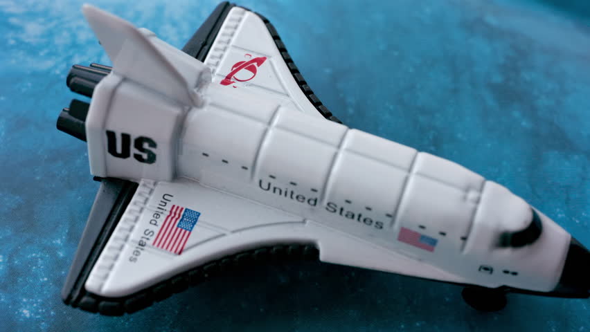 Close up of a miniature toy space shuttle placed on a blue cosmic galaxy backdrop