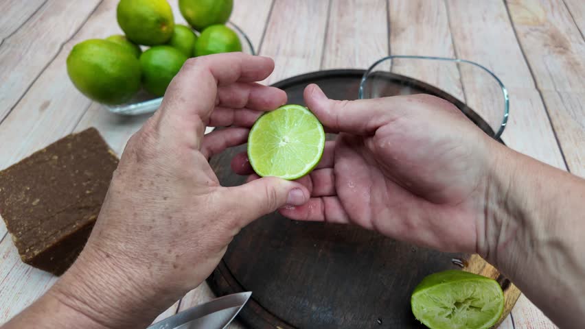Close-up POV squeezing limes into bowl, wooden surface, fresh, juicy