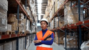 Portrait of a young african american woman in a hard hat and safety vest smiling while holding a barcode scanner inside a large distribution warehouse, with shelves full of parcels behind her - Powered by Shutterstock - Get 15% off with code: PIKWIZARD15