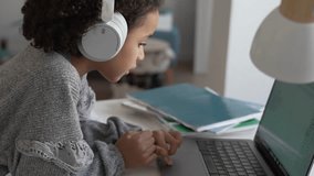 Primary school African American Student child with headphones hand writing in book using laptop. Distance learning online education. School girl studying at home with digital tablet computer and doing - Powered by Shutterstock - Get 15% off with code: PIKWIZARD15