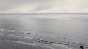 Cinematic aerial drifting above the Pacific Ocean at Arcadia Beach on the Oregon Coast as gentle waves roll in beneath low clouds with a thin blue line of sky glowing on the distant horizon. - Powered by Shutterstock - Get 15% off with code: PIKWIZARD15