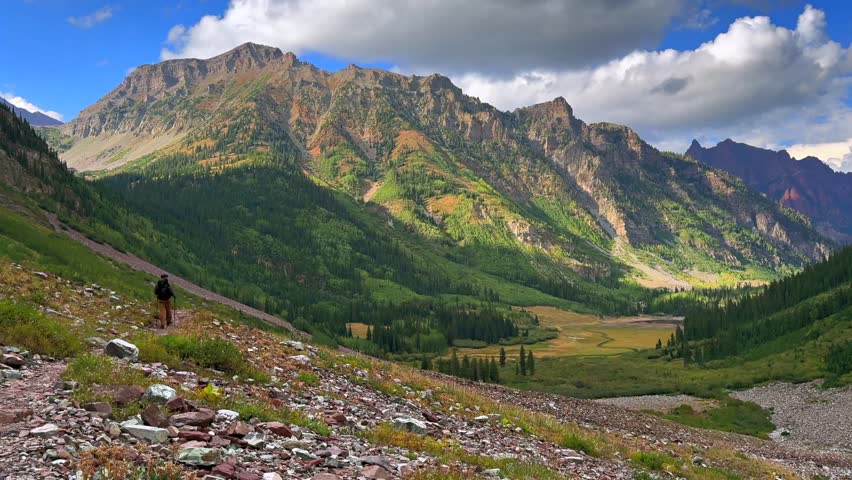 Hiking trail Maroon Bells Wilderness Maroon Crater Lake green summer valley Colorado sunny clouds movement Aspen Snowmass rugged terrain Elk Range Rocky Mountains White River Forest blue sky static