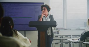 Female Coding Teacher Stands at Podium, Explaining Programming Syntax on Large Digital Screen. Concept Modern Computer Science Education, STEM Learning, Technology Literacy, and Teaching Innovation. - Powered by Shutterstock - Get 15% off with code: PIKWIZARD15