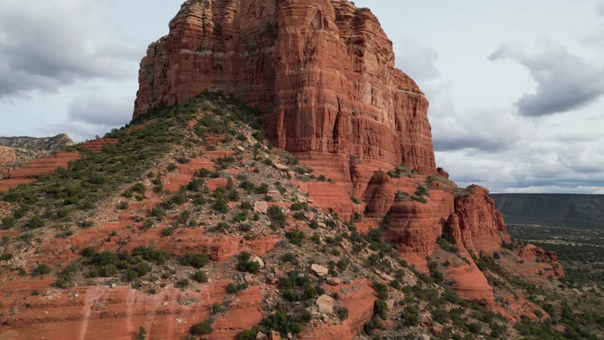Aerial drone footage of Courthouse Butte in Sedona, Arizona, highlighting towering red sandstone formation surrounded by desert landscape, cliffs, and scenic southwestern terrain under clear skies.
