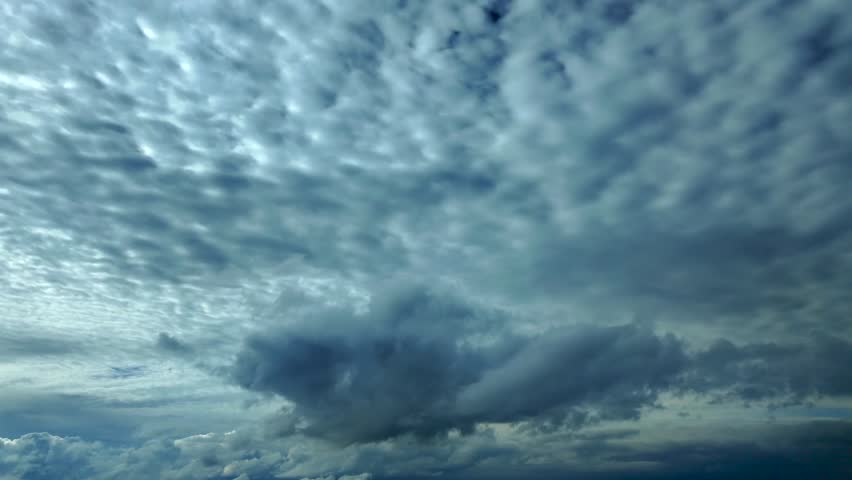 Cockpit view flying under a grey color, manacing sky, as seen by the pilots, with some cumulus clouds floating ahead.