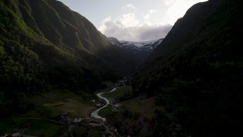 Aerial view of verdant valley and snow-capped mountains, with a winding river flowing through a village nestled below, creating a stunning contrast, Buarbreen Glacier Odda, Vestland, Norway.