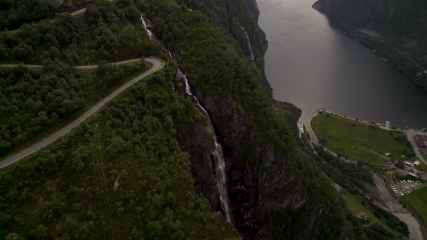 Aerial view of a winding road snaking down lush, green mountainsides towards a still, dark fjord in the landscape, Lysebotn, Rogaland, Norway.
