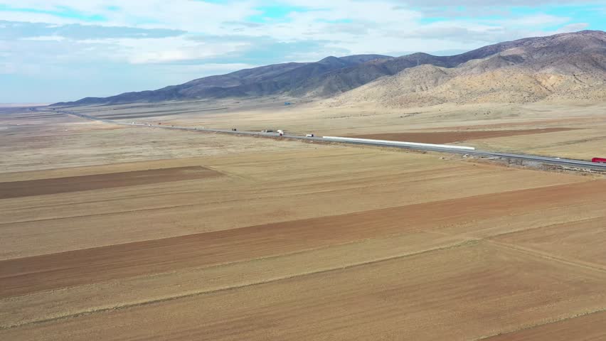 Aerial view of vast plowed fields contrasting with a long highway cutting through the landscape under a partly cloudy sky, Tuz, Ankara, Turkiye.