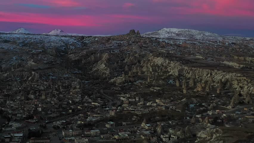 Aerial view of Goreme's surreal landscape, contrasted by a pink sky and snow-capped mountains, creating a striking scene, Goreme, Cappadocia, Turkiye. - Powered by Shutterstock - Get 15% off with code: PIKWIZARD15