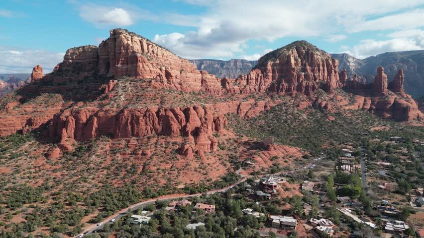 Aerial drone footage of Chapel of the Holy Cross in Sedona, Arizona, showing the modern architectural landmark built into red sandstone cliffs surrounded by desert landscape and scenic red rock views.
