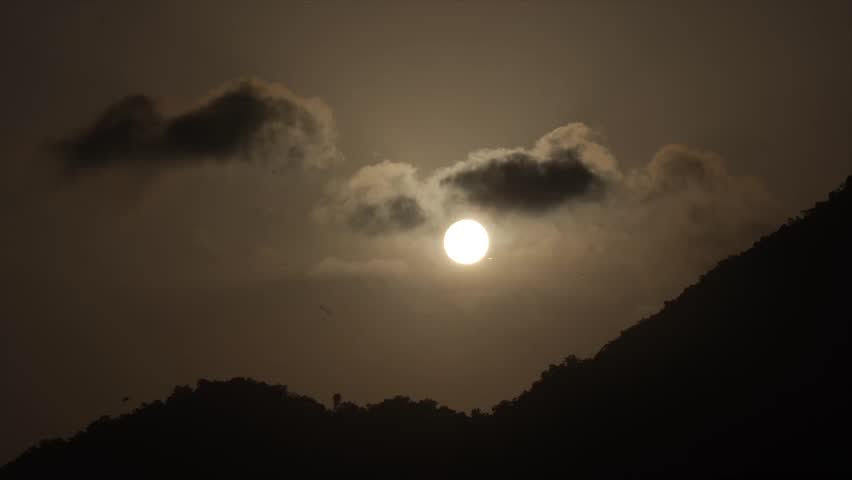 Beautiful sunset over mountain silhouette with glowing sun and dramatic clouds in the sky. Peaceful natural landscape scene shot during evening golden hour in India.