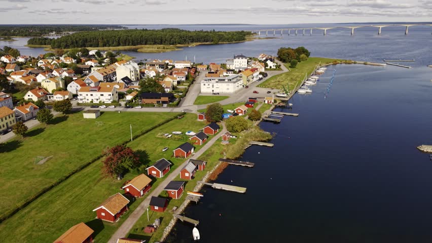 Aerial view of red-roofed houses and a distant bridge over water, with lush green fields contrasting against the deep blue sea, Kalmar, Kalmar County, Sweden.