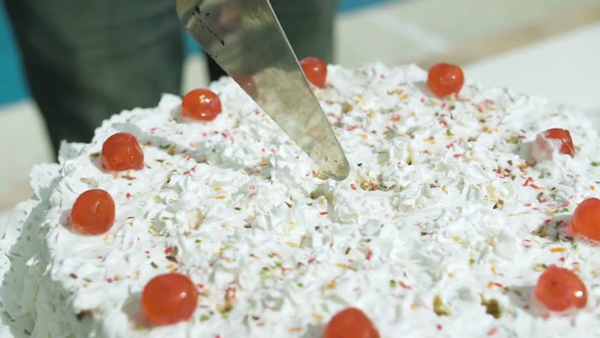 A moment of celebration as a knife slices through a moist, layered birthday cake covered in smooth, creamy frosting. The act marks a sweet beginning to the festive treat for all the guests.