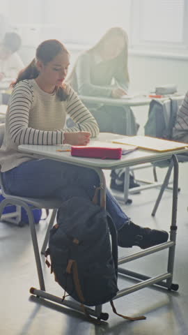 Students Writing Exam In Bright, Modern Classroom. Group of Pupils Sits at Individual Desks Focusing Intently on Taking Exam. Concentration, Independent Study, Academic Workload. Vertical Shot.