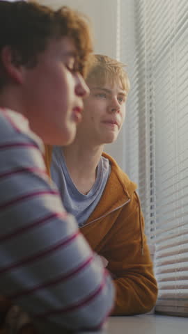 Students Lean Against Windowsill, Engaged in Calm Conversation While Gazing Through Blinds. Friendship Connection, Daydreaming, Thoughtful Communication Among Peers, Youthful Curiosity. Vertical Shot.