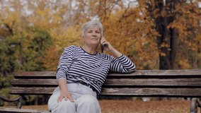 Elderly woman sitting on a bench while having an emotional phone conversation in an autumn park - Powered by Shutterstock - Get 15% off with code: PIKWIZARD15