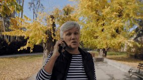 Elderly woman talking on a mobile phone while enjoying a walk in a beautiful autumn park - Powered by Shutterstock - Get 15% off with code: PIKWIZARD15