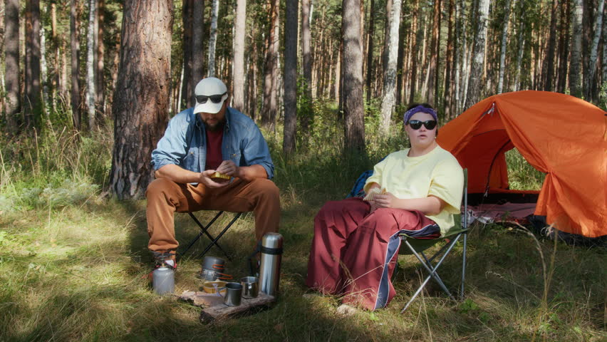 Young woman with down syndrome and man taking lunch break from hiking in camp with tent and chairs