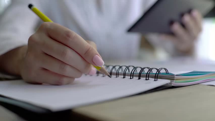 Close-up of a female hand holding a pencil and writing research notes in an appointment book, capturing productivity, study, and planning.
