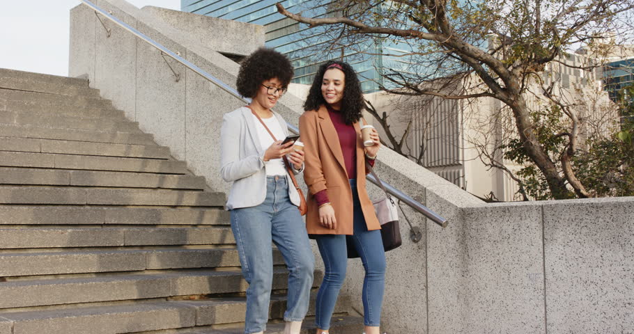 Diverse female friends glancing at smartphone while descending urban plaza stairs viewing content. Casual, friendship, urban, modern, vibrant, communication, lifestyle