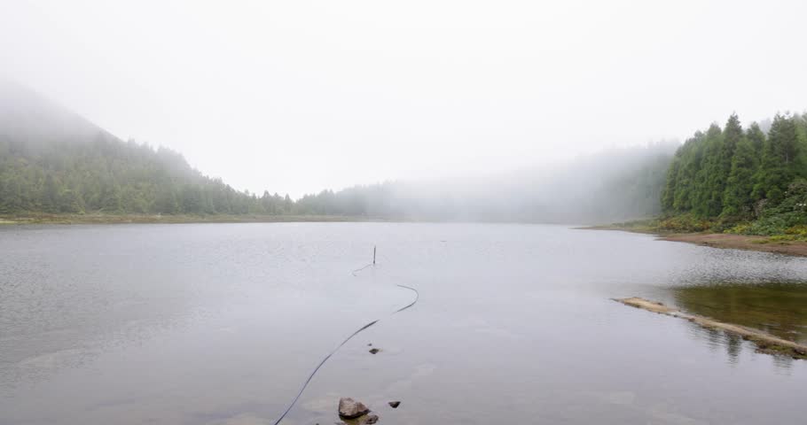 A foggy day with a lake at Lagoa Rasa and a path leading to it. The path is lined with plants and rocks. Pan left shot.
